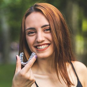 A smiling woman holding an Invisalign tray outdoors