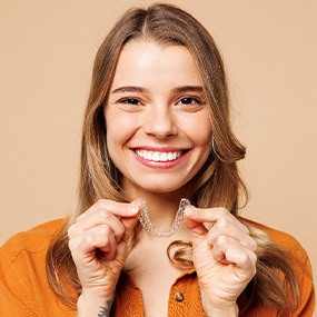 A beautiful, smiling woman holding an Invisalign tray