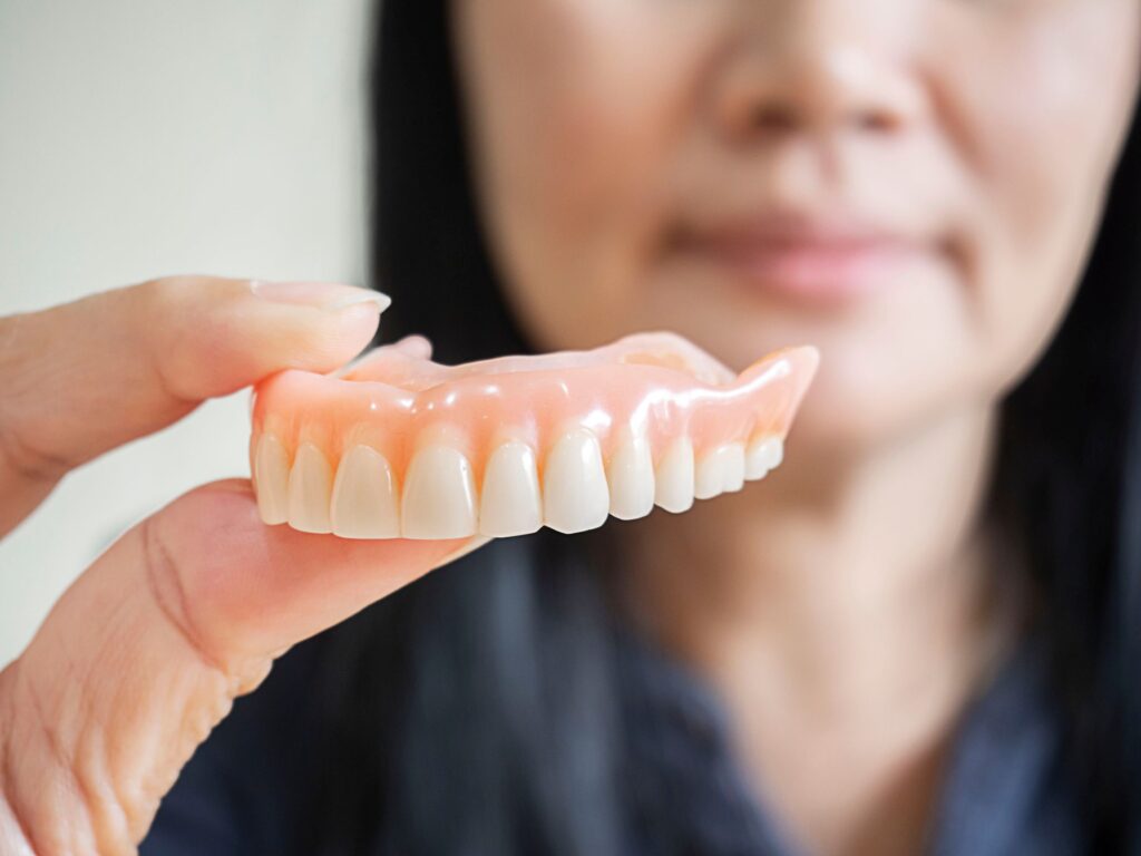 Woman blurry in background holding dentures to foreground